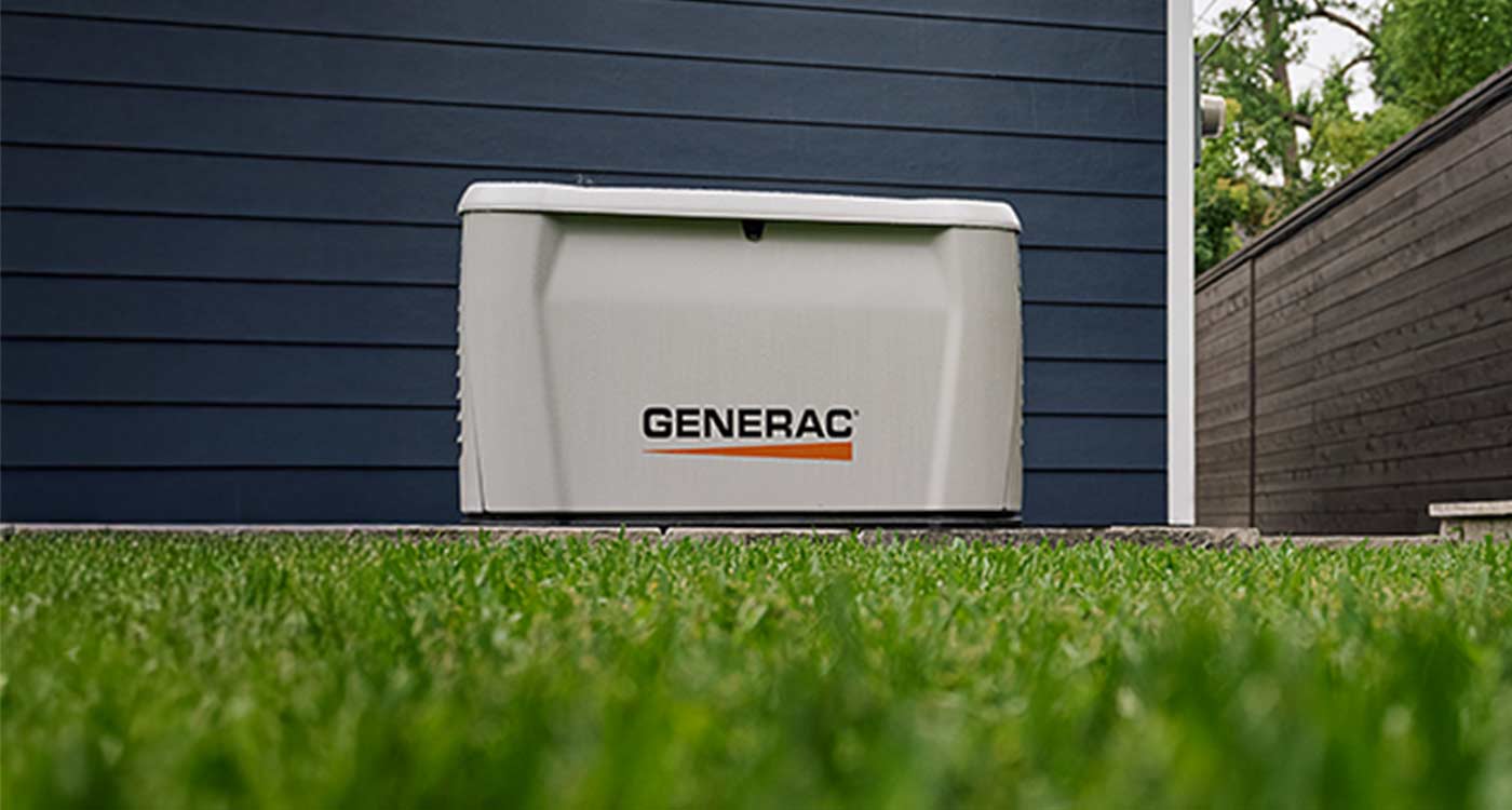 Home standby generator installed on a pad against a home's dark blue siding